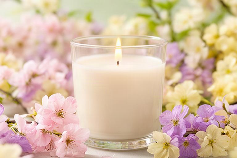 Vela aromática en vaso claro rodeada de flores primaverales de colores suaves